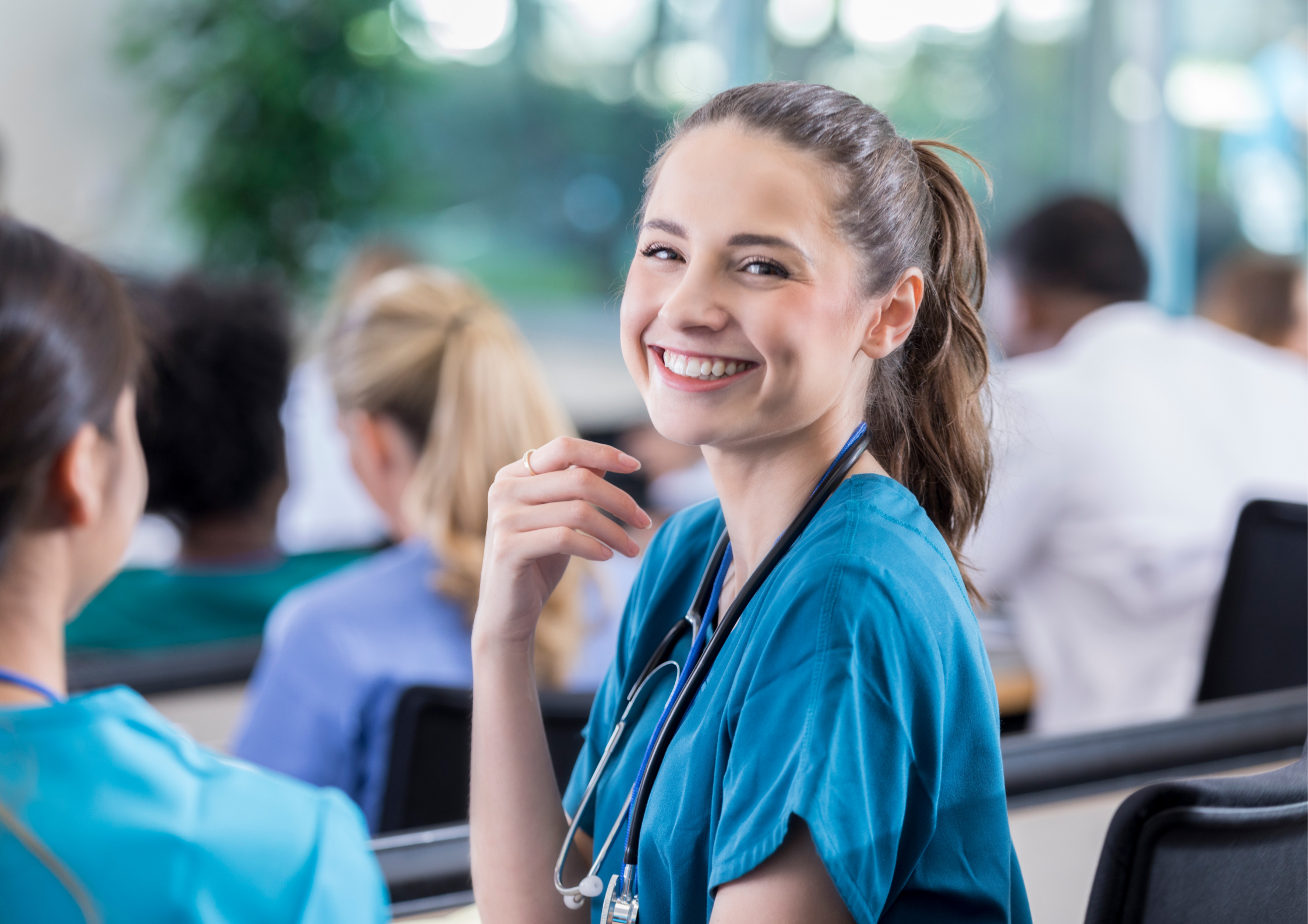 Eine junge Frau in blauer Arztkleidung und einem Stethoskop um den Hals blickt lachend in die Kamera.