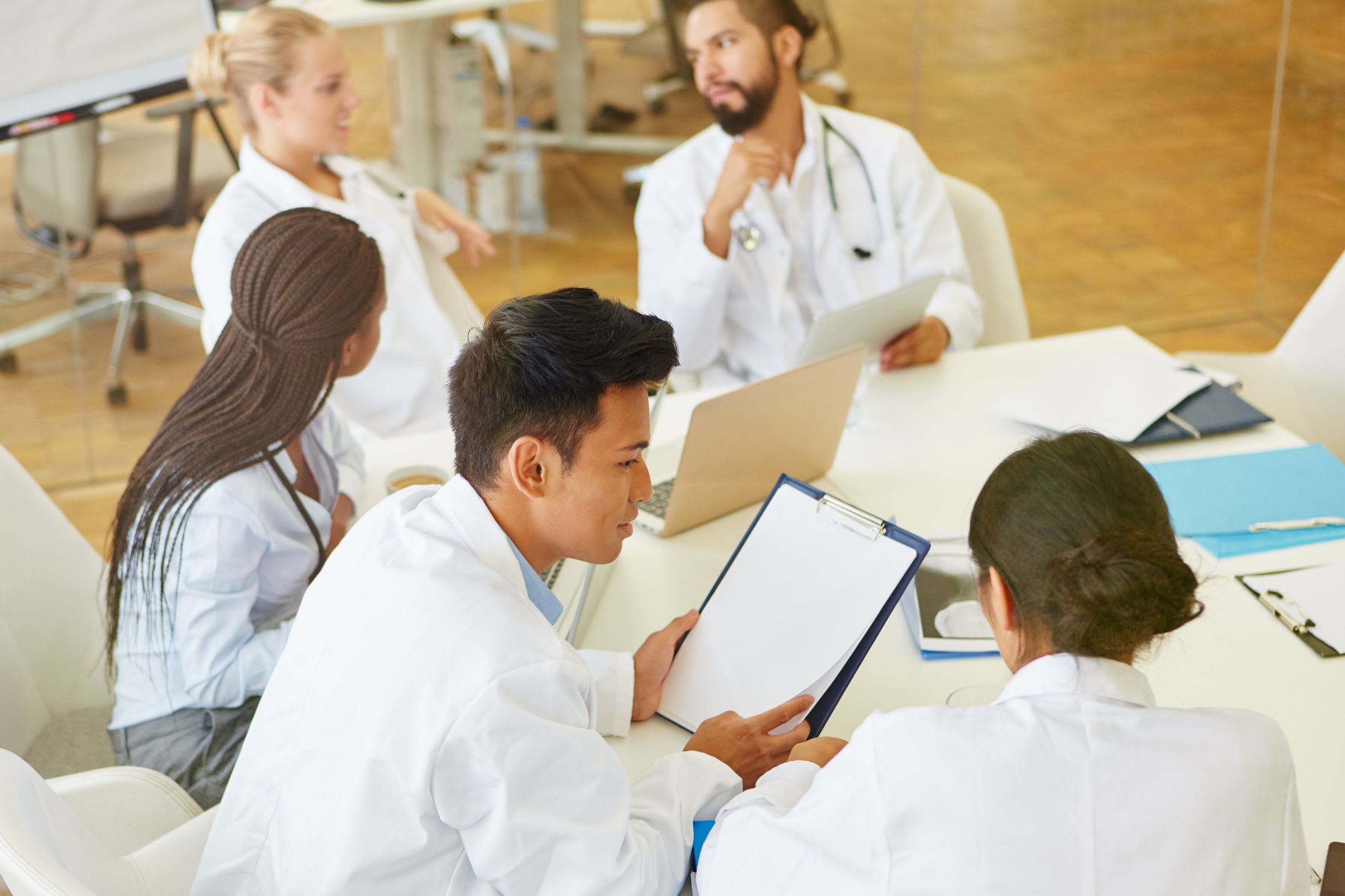 Ärzte sitzen an einem Tisch und reden über Akten und Notizen auf Klemmbrettern.