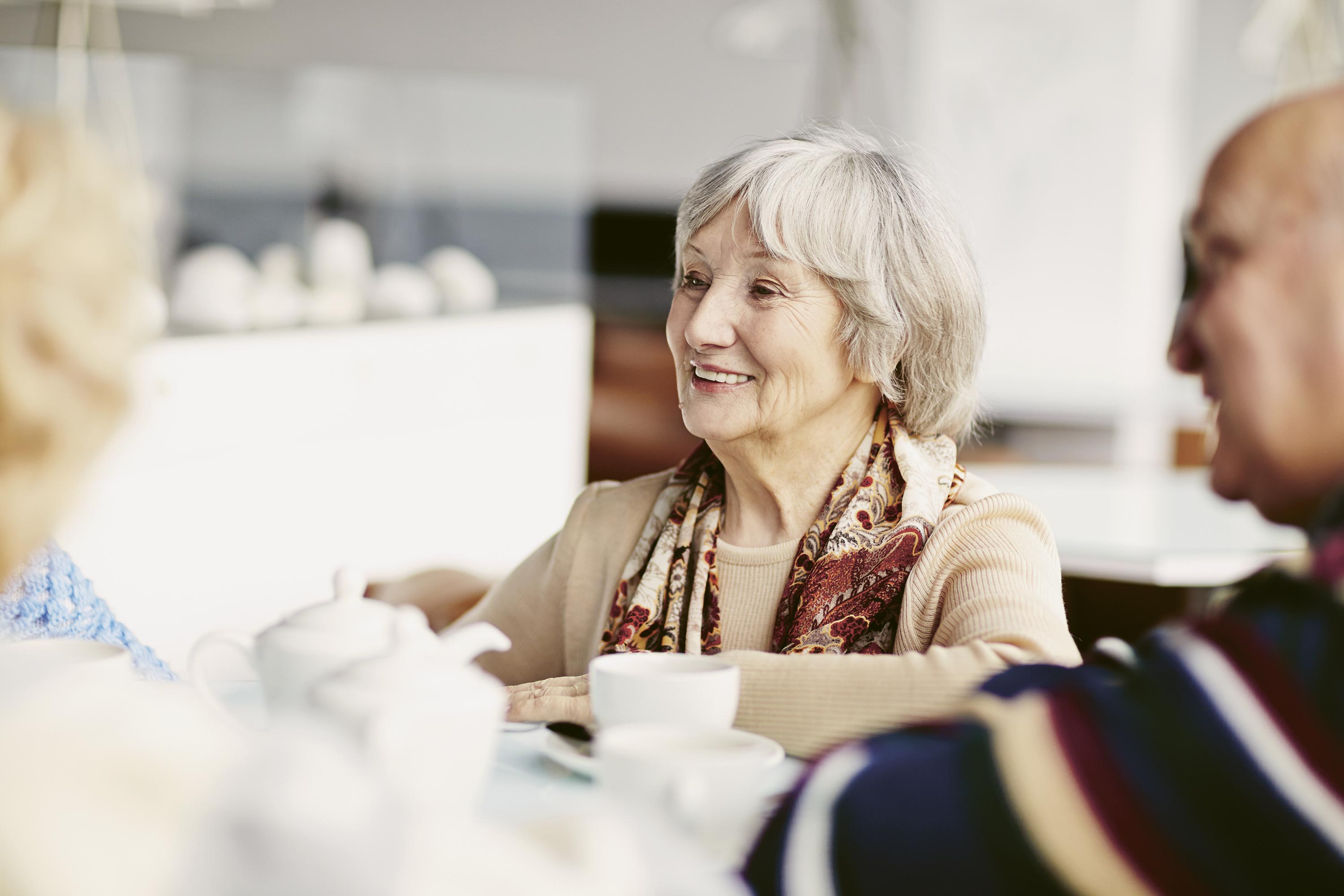 Eine ältere Frau sitzt an einem Kaffeetisch.
