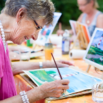 Eine ältere Frau malt mit Wasserfarben und ist glücklich.