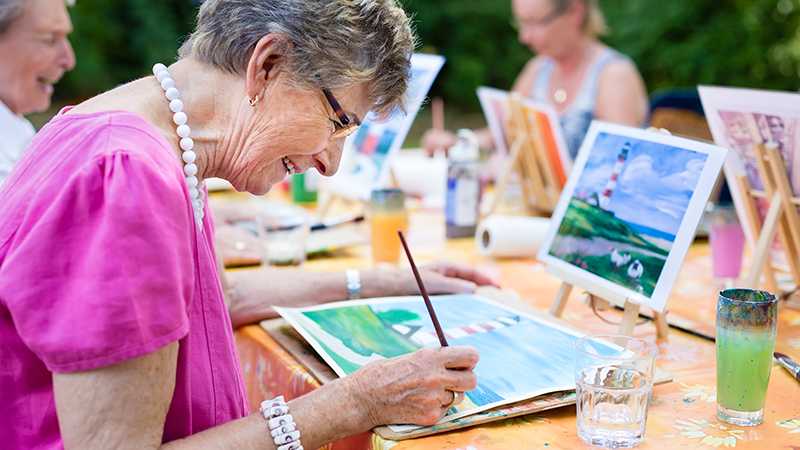 Eine ältere Frau malt mit Wasserfarben und ist glücklich.