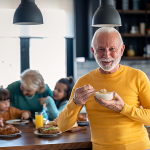 Glücklicher, zufriedener älterer Mann blickt in die Kamera, während er Haferbrei zum Frühstück isst