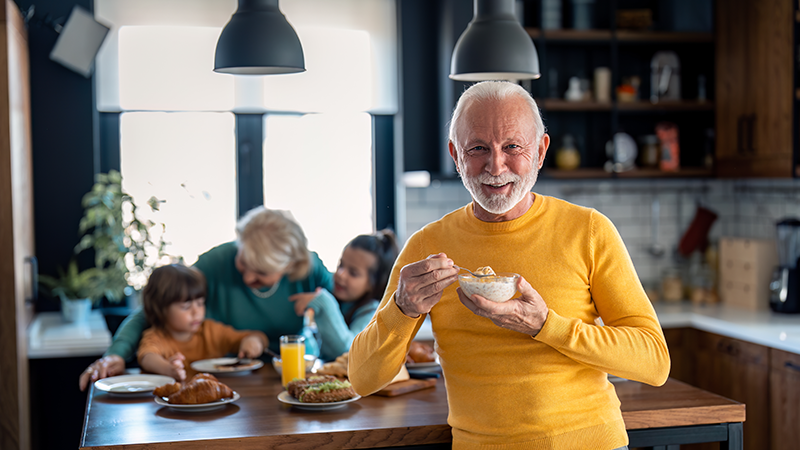 Glücklicher, zufriedener älterer Mann blickt in die Kamera, während er Haferbrei zum Frühstück isst