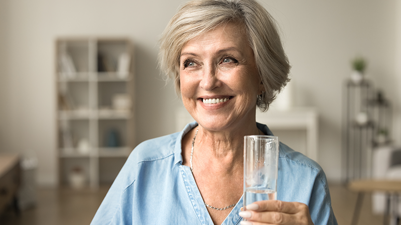 Eine Frau hält ein Glas Wassser und lächelt