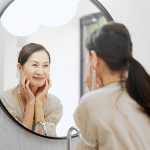 Frau betrachtet sich skeptisch im Spiegel