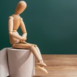 Holzpuppe sitzt auf Toilettenpapierrolle und symbolisiert Darmbeschwerden