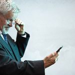 Älterer Geschäftsmann muss Smarphone weit weg halten, weil er altersweitsichtig ist.