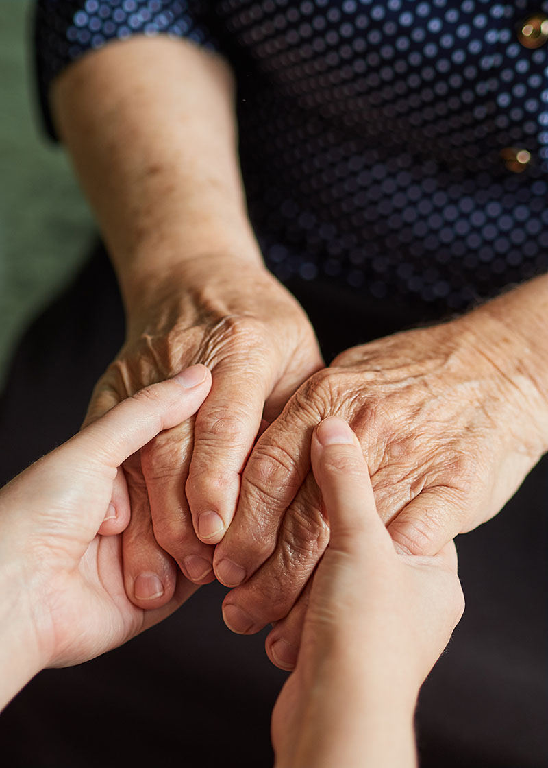 Hands of a young and old woman are holding together on a dark background Berührung im Alter - sich berührende Hände