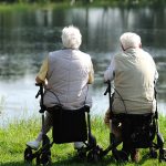 Zwei ältere Menschen sitzen auf Rollatoren und blicken auf einen See