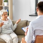 Ältere Frau lässt sich auf einem Sofa von einem Sozialtherapeuten beraten