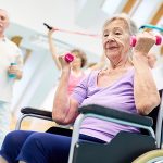 Ältere Frau im Rollstuhl versucht vorsichtig leichte Gewichte zu heben