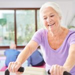 Ältere Frau auf dem Crosstrainer trainiert lächelnd und motiviert