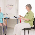 Die Ergotherapeutin erklärt Patientin wie die Sockenanziehhilfe funktioniert