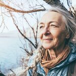 Ältere Frau steht in der Natur und sieht glücklich aus.